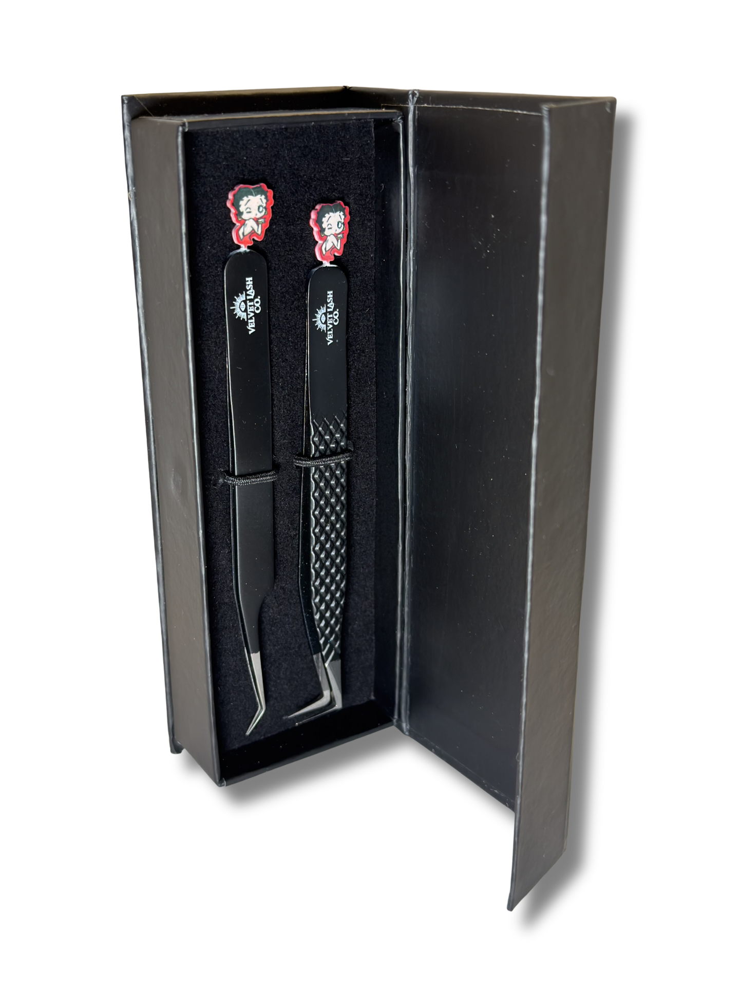 Two metal tools with red handles in a black box on a white background. Betty Boop Lash Tweezer kit.