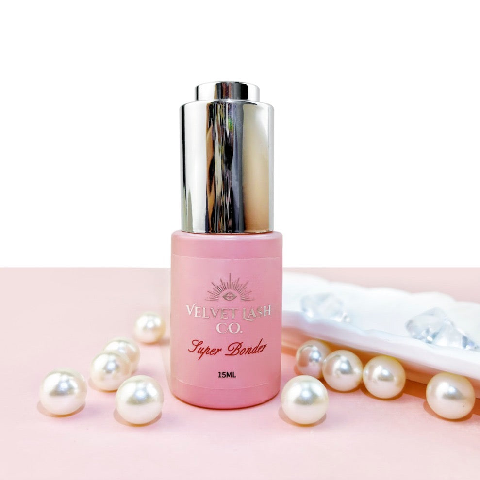 Pink bottle with silver cap on a pink background with pearls, lash bonder for lash extensions by Velvet Lash Co 