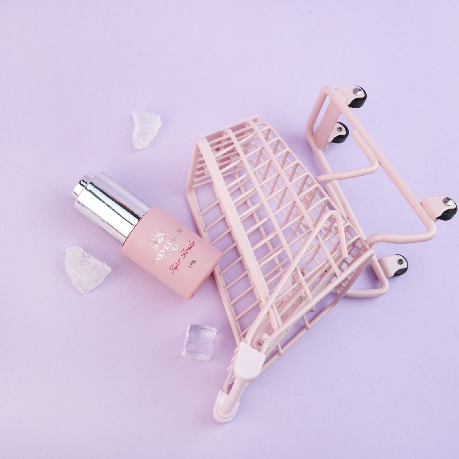 Pink lash bonder bottle with a small pink shopping cart on a light purple background
