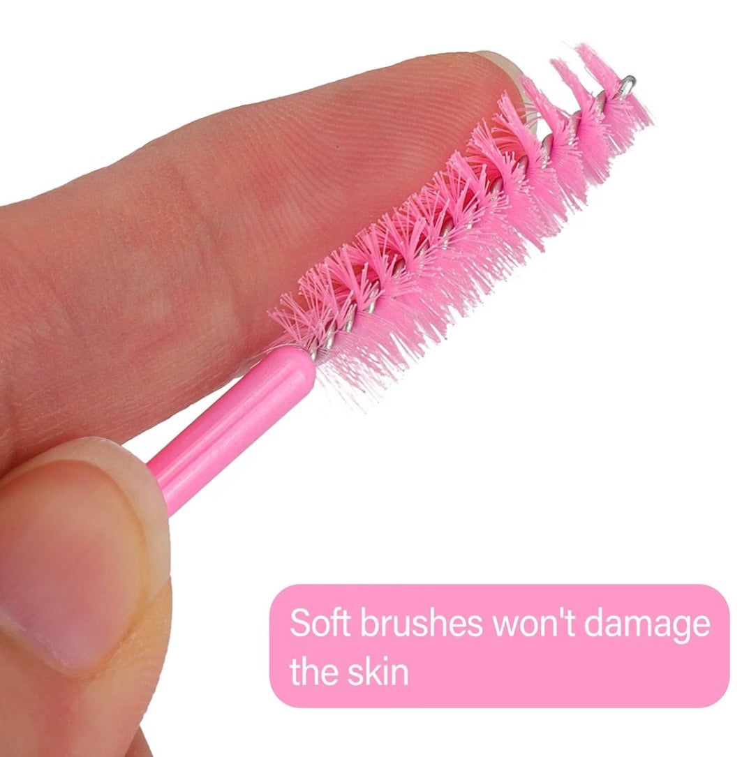 A close-up of a small pink beauty brush being held between fingers, with soft bristles and a metal loop at the end. A pink text box at the bottom reads, 'Soft brushes won't damage the skin.